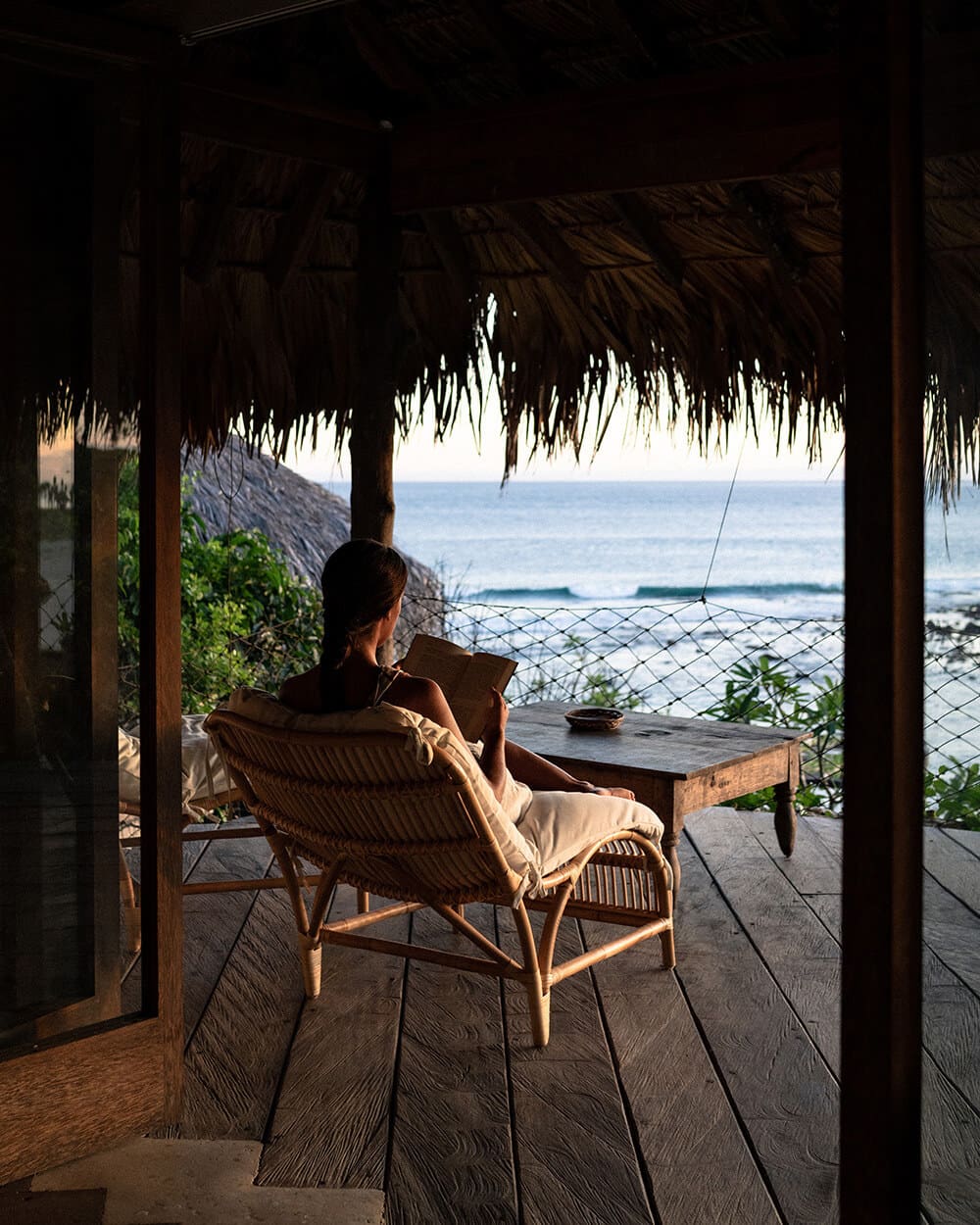A girl sits reading a book on her bungalow balcony overlooking the ocean at Boa Vida Rote.